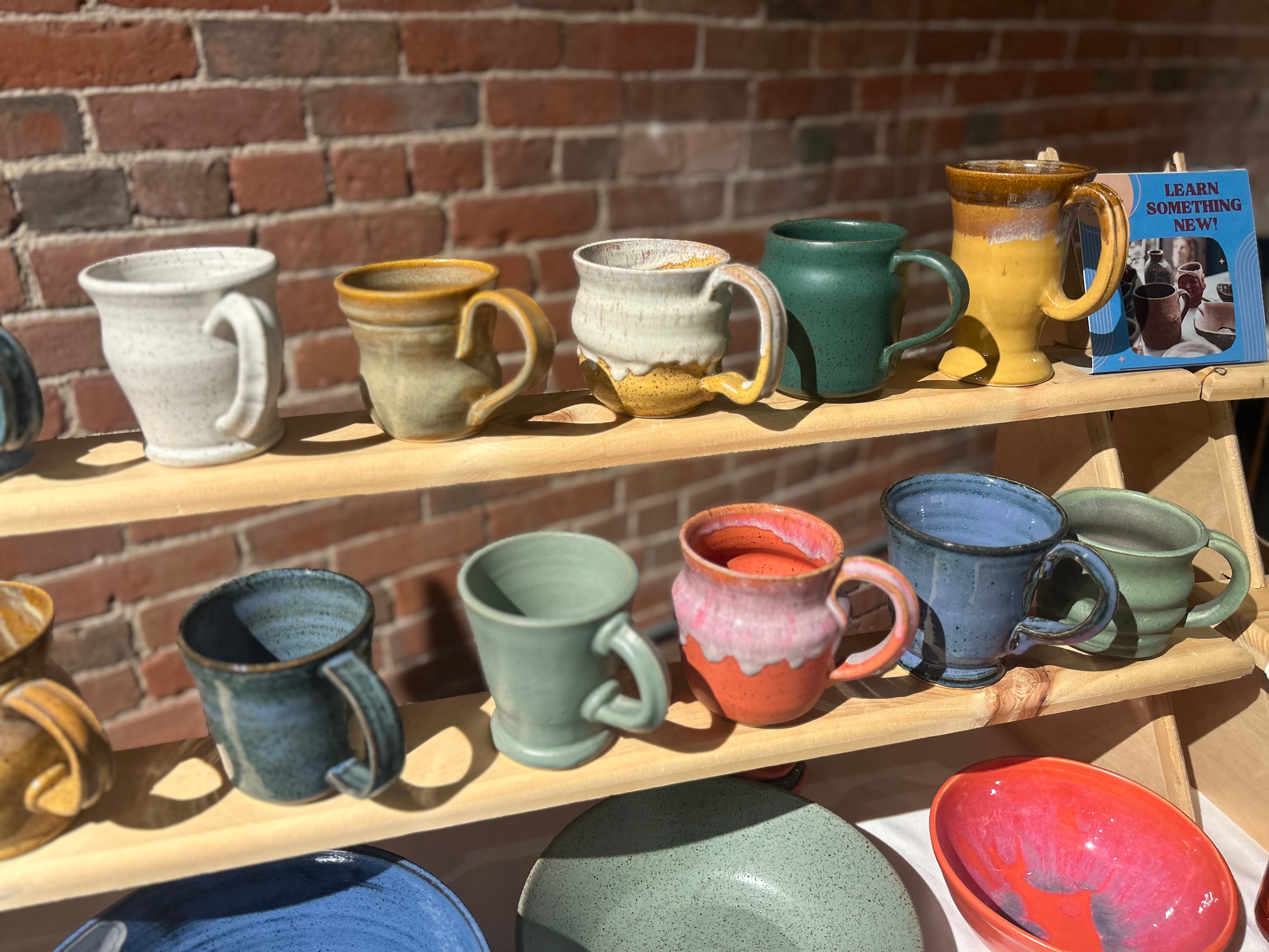Collection of ceramic mugs and bowls on wooden shelves against a brick wall.
